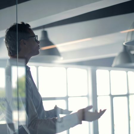 Business professional giving a presentation in a modern office setting through glass.