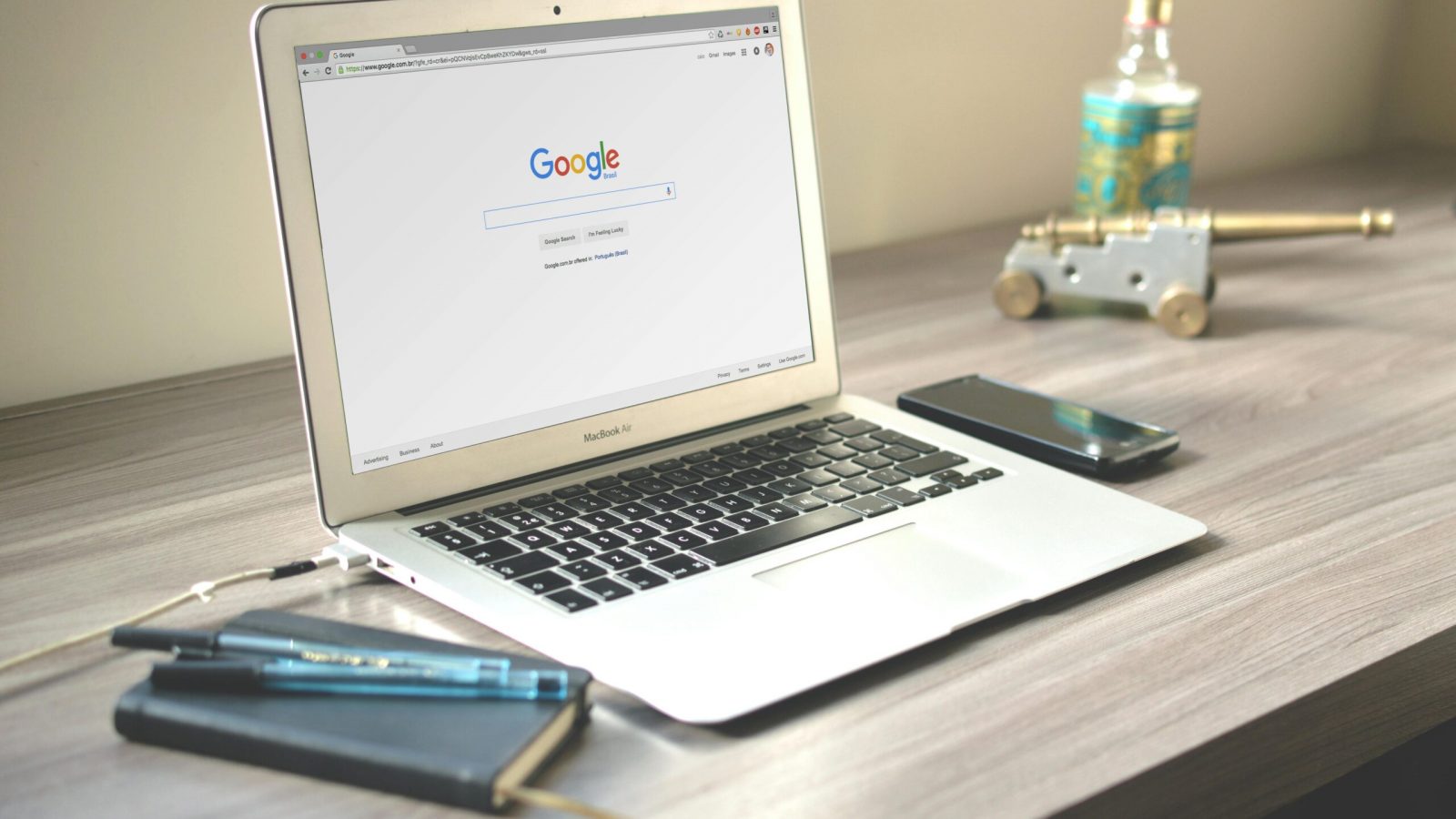 A neat workspace featuring a laptop displaying Google search, a smartphone, and a notebook on a wooden desk.